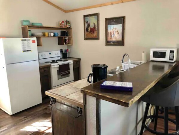A kitchen with a refrigerator, stove, microwave, and a bar area with stools. - Cottonwood Creek Cabins - Entire Site (Alpine)