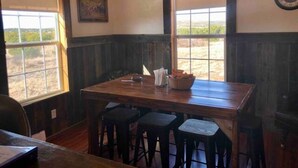 A rustic dining area with a wooden table and bar stools, large windows with a view of the outdoors, and a clock on the wall. - Cottonwood Creek Cabins - Entire Site (Alpine)