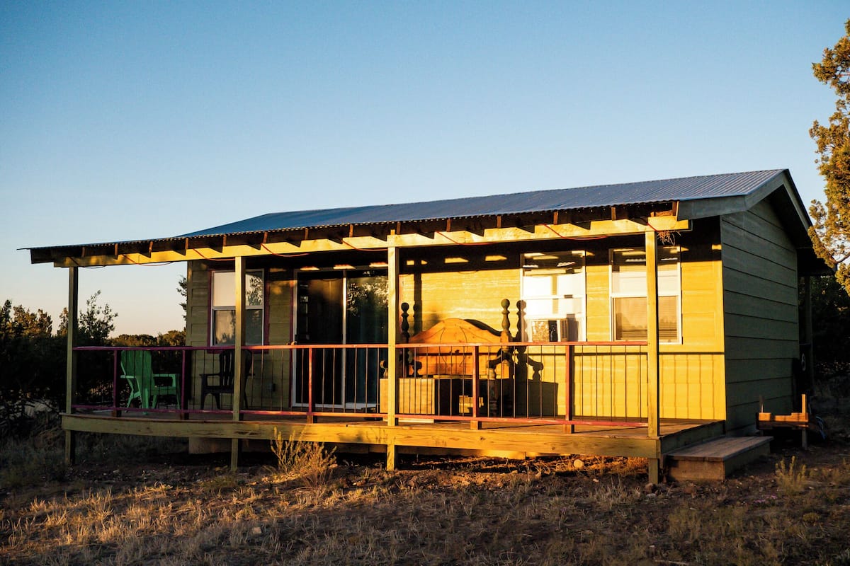 Une maison en bois dotée d’un porche abrité, de grandes fenêtres et d’une terrasse délimitée par une clôture.
