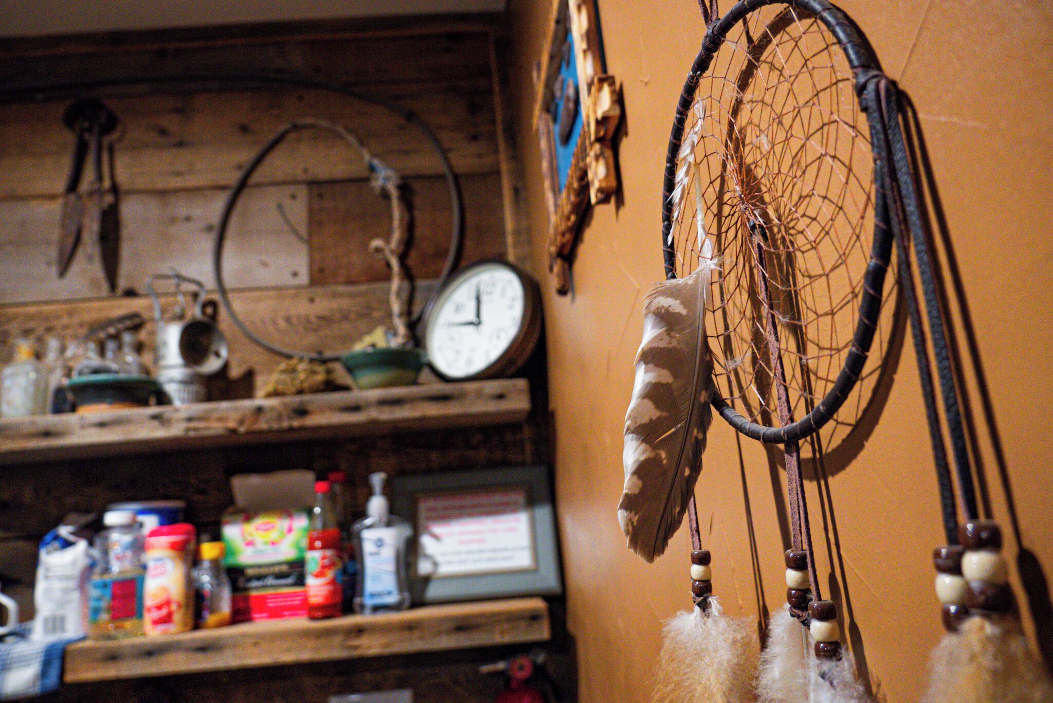 A rustic kitchen with wooden shelves holding various kitchen items and a dreamcatcher hanging on the wall.