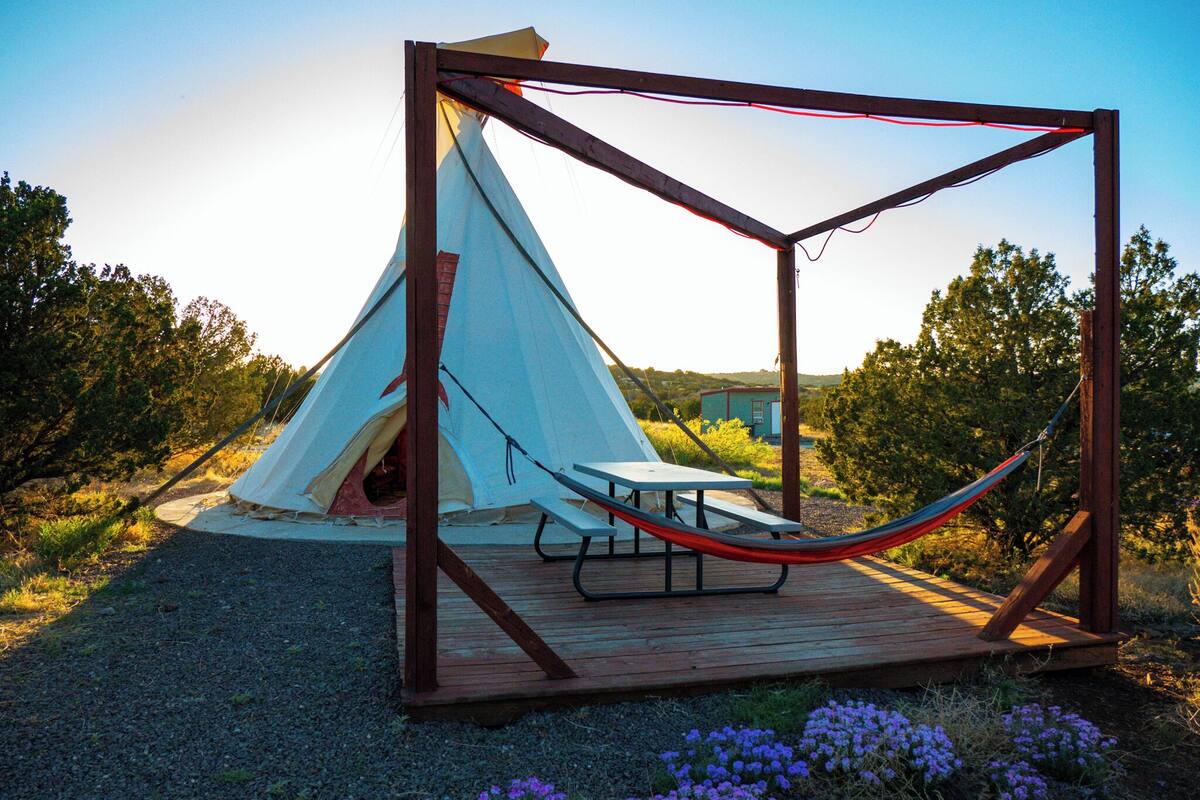 Une terrasse en bois avec un hamac, une table de pique-nique et une tente.