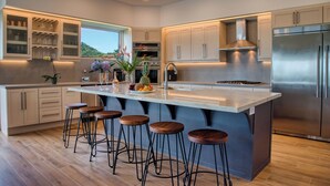 A modern kitchen with a large island, bar stools, stainless steel appliances, and a view of the outdoors. - Casa Colochos at Los Suenos Resort (Playa Herradura)