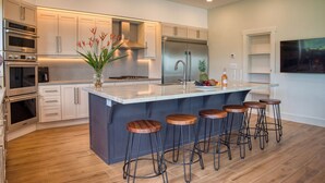 A modern kitchen with stainless steel appliances, a marble island, and bar stools. - Casa Colochos at Los Suenos Resort (Playa Herradura)