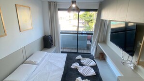 Een hotelkamer met een bed, een televisie, een raam met uitzicht op de straat en een plafondlamp.