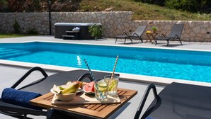 A poolside setting with a table set for two, featuring a fruit platter and drinks.