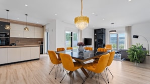 A modern kitchen with a central island, a dining area with a black table and yellow chairs, and a living area with a sofa and a large plant.