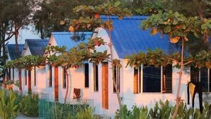 A row of white buildings with blue roofs and wooden shutters, surrounded by greenery and a paved path. - Blue Marine Resort (Saint Martin's Island)