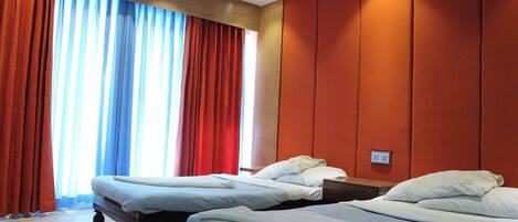 A hotel room with two beds, a wooden ceiling, and a large window with red curtains.
