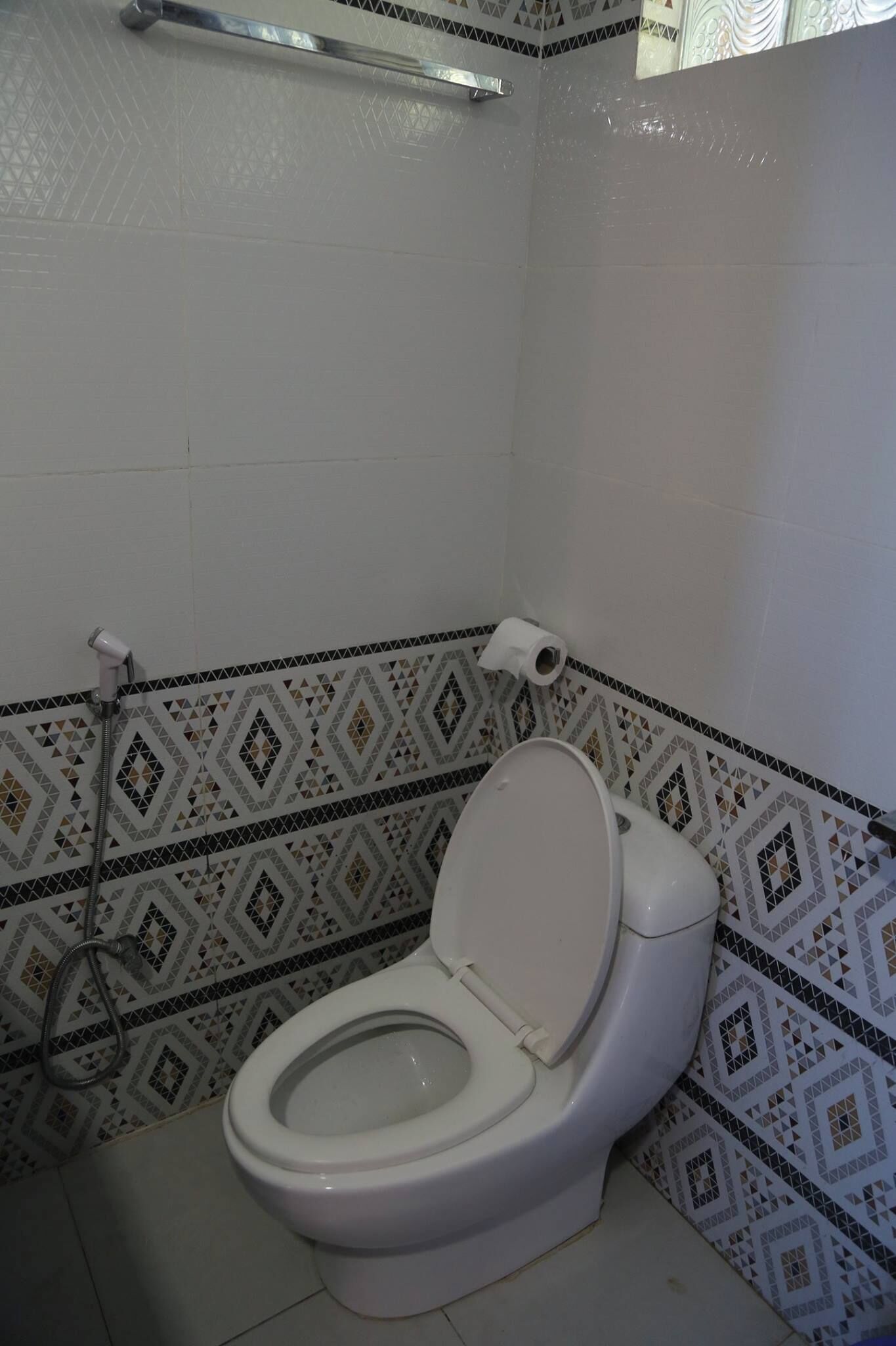 Ein Badezimmer mit Toilette, Dusche und gemusterten Fliesen.