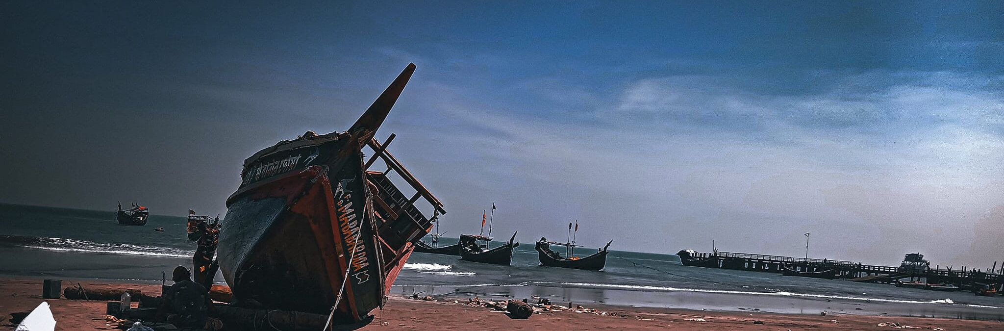 Een strand met verschillende boten, waaronder een grote omgekeerde boot op de voorgrond en kleinere bootjes in het water.