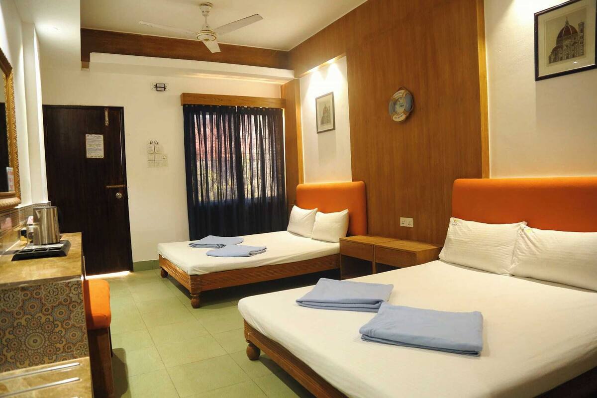 Habitación de hotel con dos camas, cabecero de madera, una mesita con hervidor y ventana con cortinas.