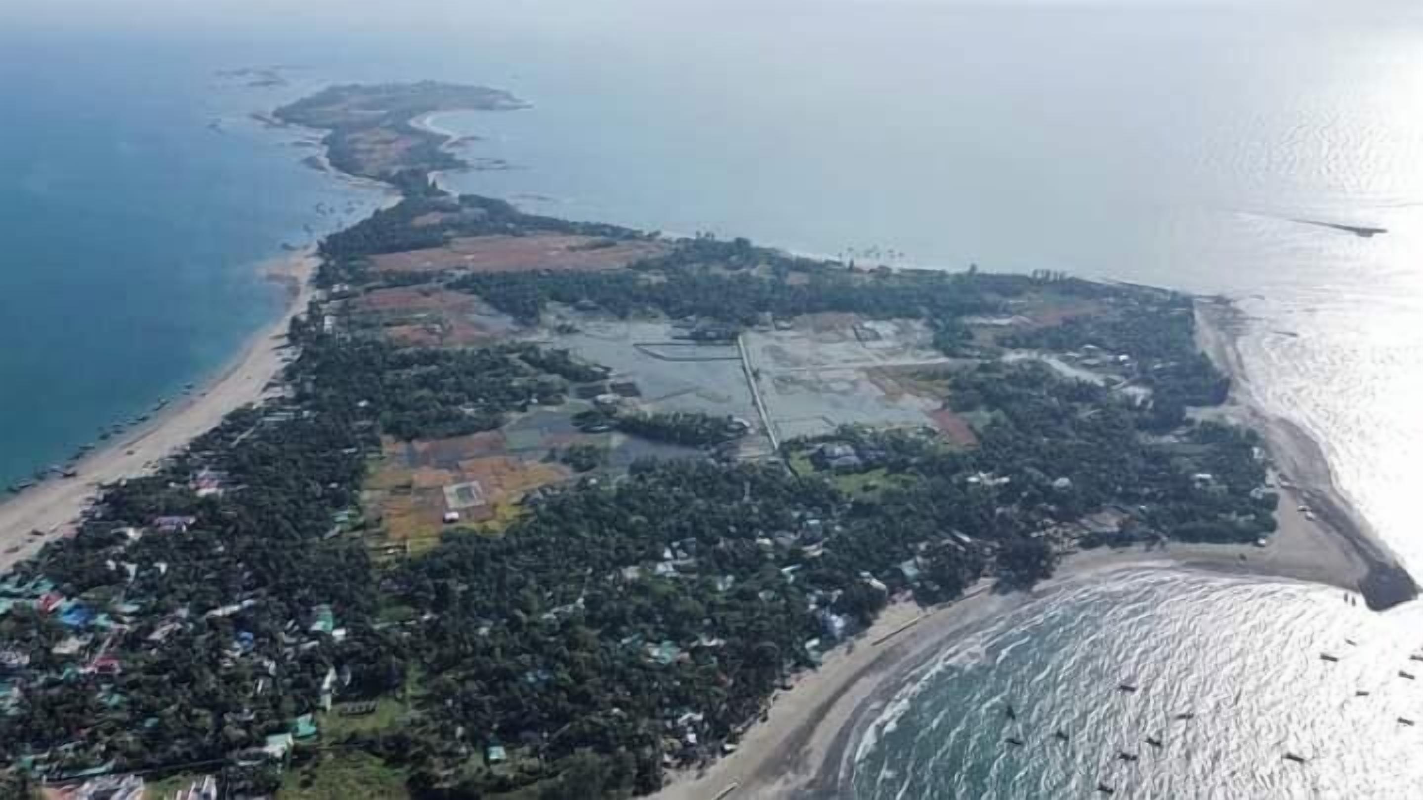 An aerial view of a coastal area with a beach, dense vegetation, and a mix of residential and undeveloped land.