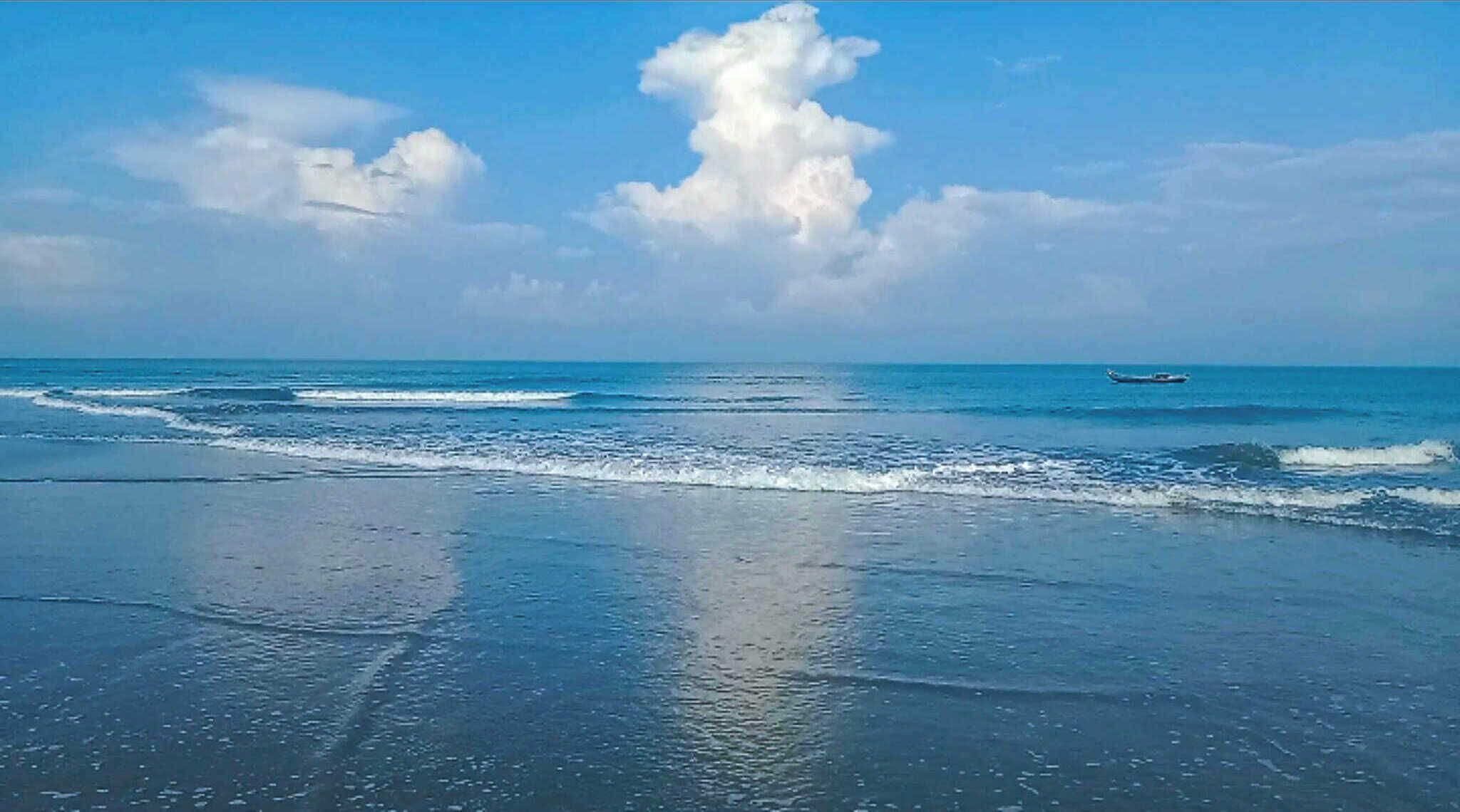 A beach with waves, a boat in the distance, and a clear sky.