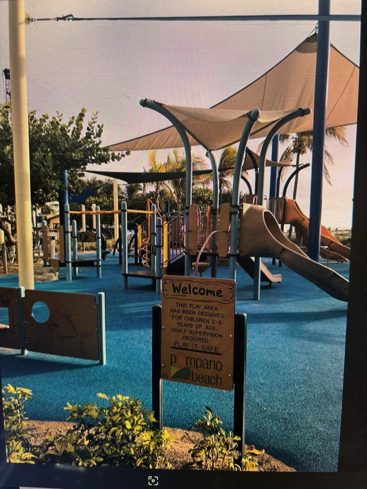 A playground with various play equipment, including slides and climbing structures, under a shaded area.
