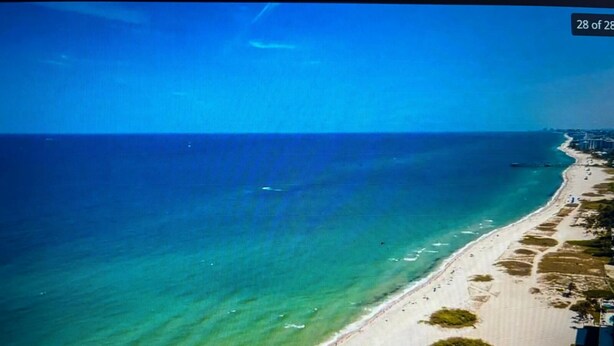 Vista aérea de una playa con aguas turquesas cristalinas, una orilla arenosa y algunos edificios a lo largo de la costa.