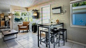 Una cocina moderna con comedor, un televisor montado en la pared y una ventana con vistas a la vegetación.