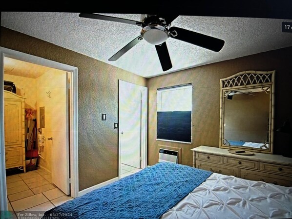 Een slaapkamer met een bed, een plafondventilator, een raam, een spiegel en een dressoir.