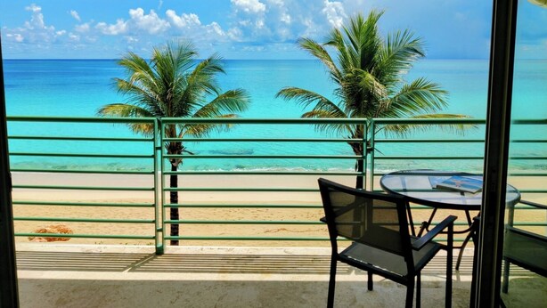 Un balcon avec vue sur l’océan, deux palmiers et une table avec des chaises.
