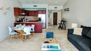 Un salon moderne avec un canapé foncé, une table basse et un coin repas comprenant une table et des chaises blanches.