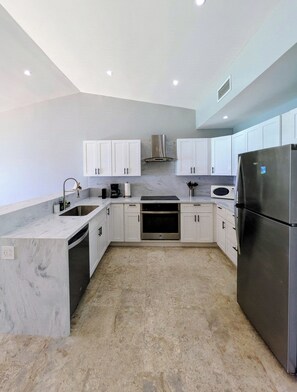 A modern kitchen with white cabinets, a stainless steel refrigerator, and a built-in oven. - ☀️⛱️👙Shore Thing by IRE Vacations- Beachfront 1 Bedroom Condo in Simpson Bay (Simpson Bay)