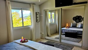 Une chambre à coucher avec un lit, une table de chevet avec une lampe, et une vue sur une autre pièce accessible par une porte coulissante.