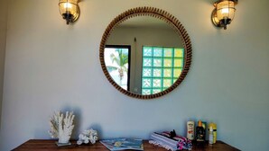 A wooden vanity with a round mirror, two wall-mounted lights, and a window with a view of palm trees. - ☀️⛱️👙Shore Thing by IRE Vacations- Beachfront 1 Bedroom Condo in Simpson Bay (Simpson Bay)