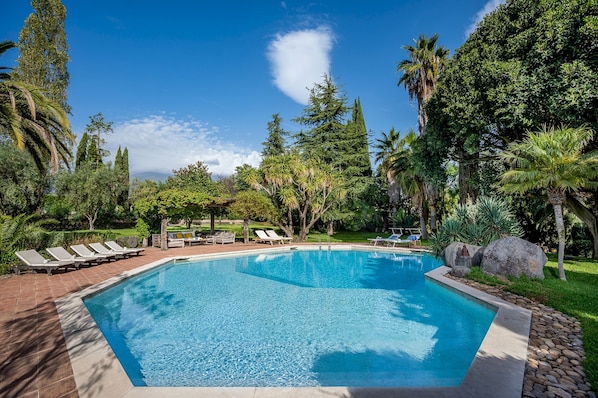 A rectangular swimming pool with clear blue water, surrounded by a tiled deck and lounge chairs.
