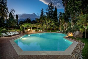A swimming pool with lounge chairs and a pergola, surrounded by trees and rocks.