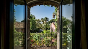 Uitzicht door een glazen deur op een tuin met een pannendak, een palmboom en een hek.