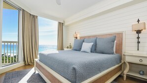 Un dormitorio con una cama grande, un ventilador de techo, una mesita de noche con lámpara y vista al océano.