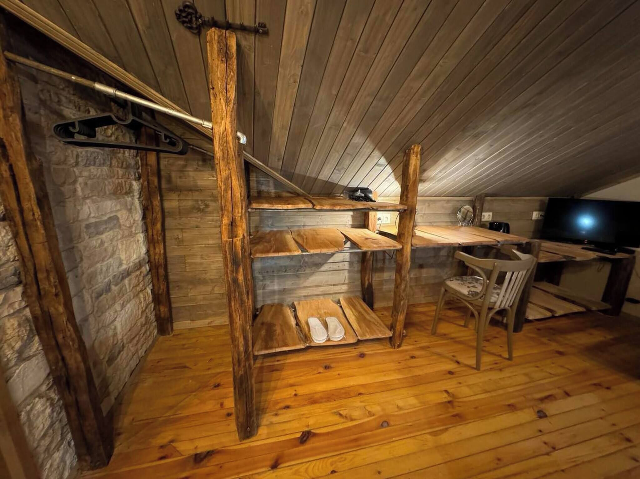 A cozy attic bedroom with a wooden bunk bed, a desk, and a television.