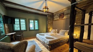 Une chambre à coucher rustique avec un grand lit, un plancher en bois et un mur en pierre. Elle comprend deux fenêtres et une petite table avec une chaise.