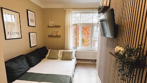 Une chambre à coucher avec un lit, un téléviseur fixé sur un panneau en bois et des tableaux encadrés au mur.