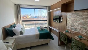 Hotellihuone, jossa on sänky, sohva, ruokapöytä tuoleineen, televisio ja näkymä kaupungin ylle.