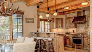 A rustic kitchen with wooden cabinets, a large stove, and a dining area with stools. - Luxurious Moonlight Basin Chalet! Stunning Views with Private Deck with Grill an (Big Sky)