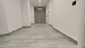 A hallway with a herringbone-patterned floor, white walls, and a ceiling with recessed lighting. - Sweet Rooms San Francesco (Naples)