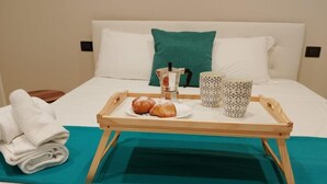 A neatly made bed with a teal bedspread, a tray with pastries, a coffee pot, and two patterned mugs. - Sweet Rooms San Francesco (Naples)
