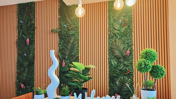A reception desk with a 'Welcome' sign, potted plants, and a wooden slat wall. - Sweet Rooms San Francesco (Naples)