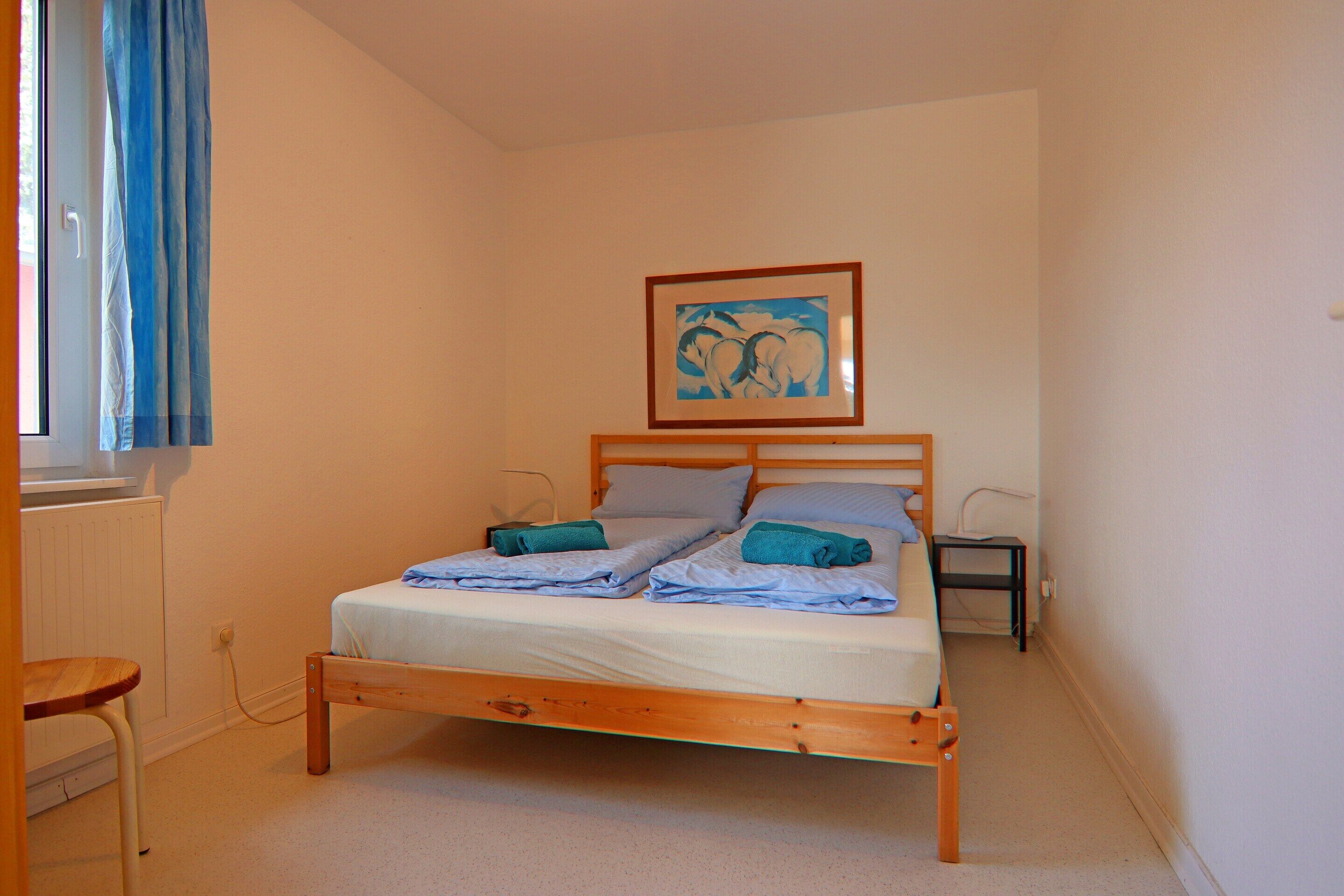 A single bed with a wooden frame, a bedside table, a nightstand, and a framed picture on the wall.