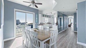 Een moderne keuken met witte kasten en een groot eiland, een eetgedeelte met witte stoelen en een stadszicht door grote ramen.
