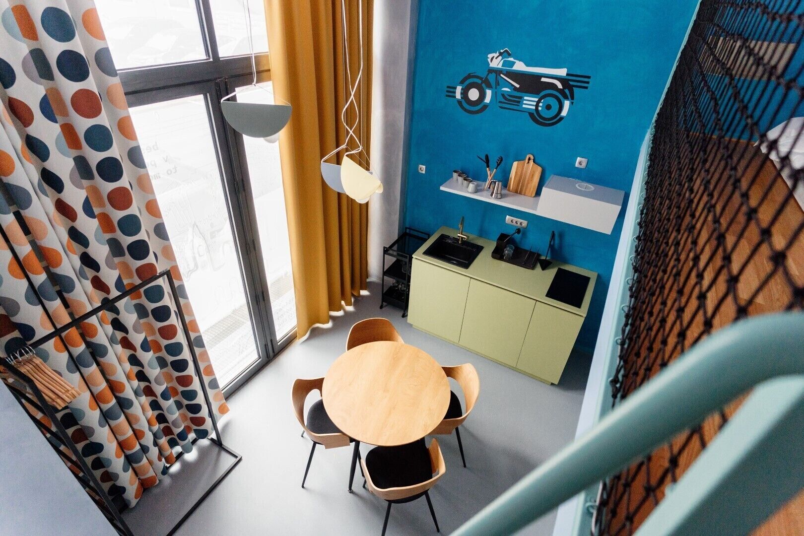 A modern kitchen with a blue wall, a yellow curtain, and a dining area with a round table and chairs.