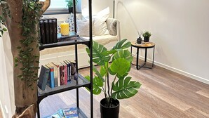 A modern living room with a wooden bookshelf, a potted plant, and a round mirror on the wall. - Elegant new building between Hamburg & Lübeck, Baltic Sea with parking lot in Reinfeld (Reinfeld)