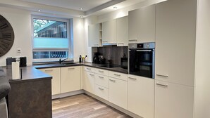 A modern kitchen with white cabinets, a built-in oven, and a large window. - Elegant new building between Hamburg & Lübeck, Baltic Sea with parking lot in Reinfeld (Reinfeld)