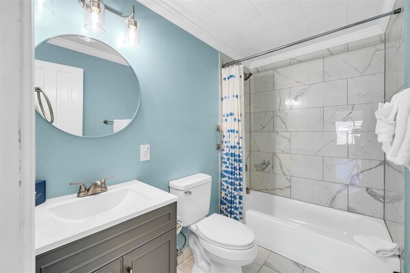 A bathroom with a white sink, toilet, and bathtub, a blue shower curtain, and a mirror with lights. - CHARMING 3/2 PET FRIENDLY! PRIVATE POOL AND HOT TUB! (Panama City Beach)