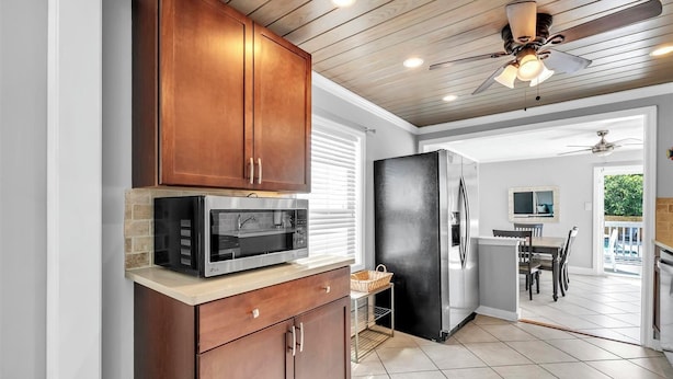 Una cocina con armarios de madera, microondas, refrigerador y ventilador de techo.