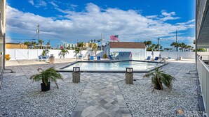 A rooftop pool area with a flag, lounge chairs, and a small building. - Spectacular Ocean View STEPS from the Beach and Pool! Third Floor Studio! (New Smyrna Beach)