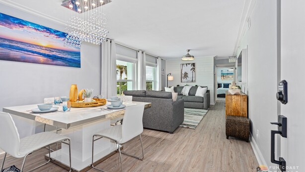 A modern living room with a dining area, a gray sofa, and a large painting of a sunset.