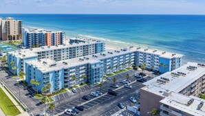 A multi-story hotel with a rooftop pool, parking lot, and ocean view.