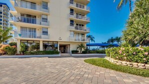 A multi-story hotel with balconies, a paved entrance area, and a landscaped garden with flowers.