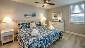 A bedroom with a bed, nightstands, a ceiling fan, a dresser, and a window with blinds.